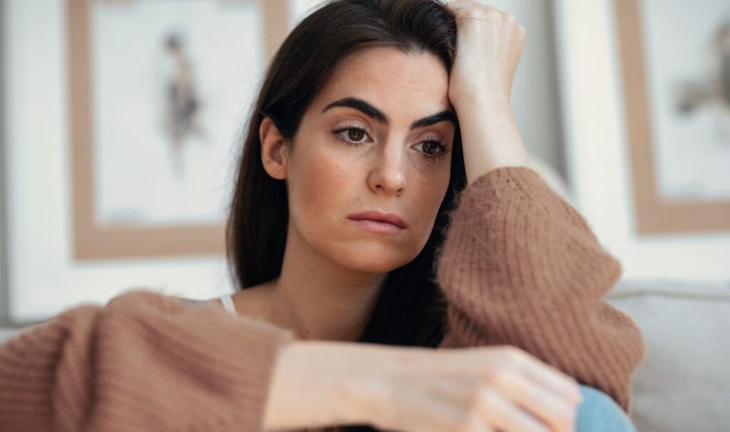a sad woman sitting on a sofa and ruminating on how she can use mindfulness for overthinking which is causing her problems.