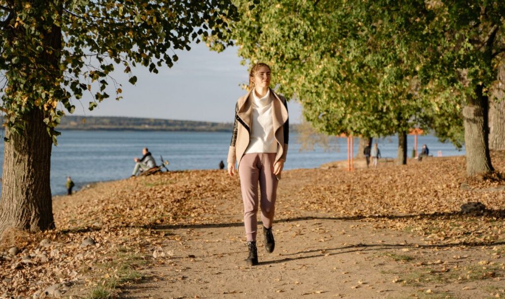 A young woman practicing walking meditation on a narrow path in nature next to the lake.