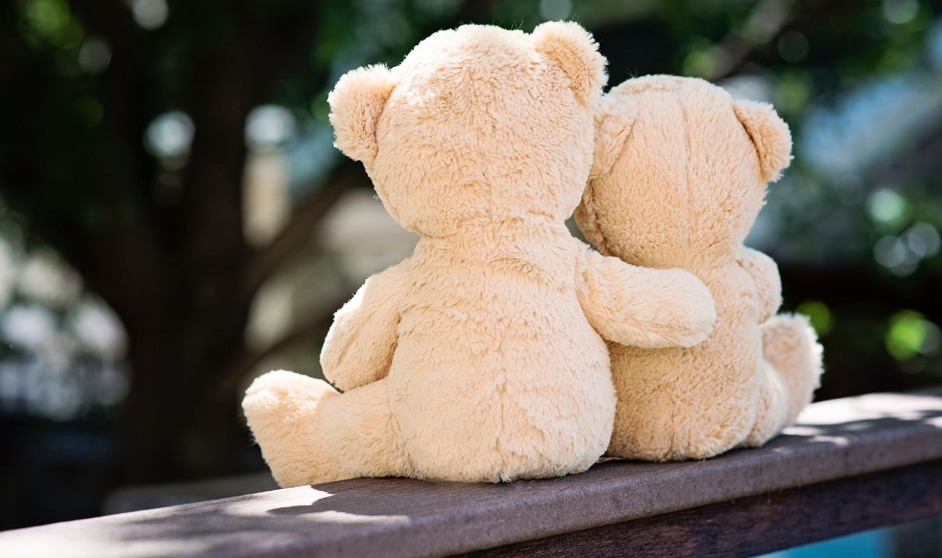 Two teddy bears sitting together and hugging on a bench, symbolizing love, connection, and manifesting a specific person.