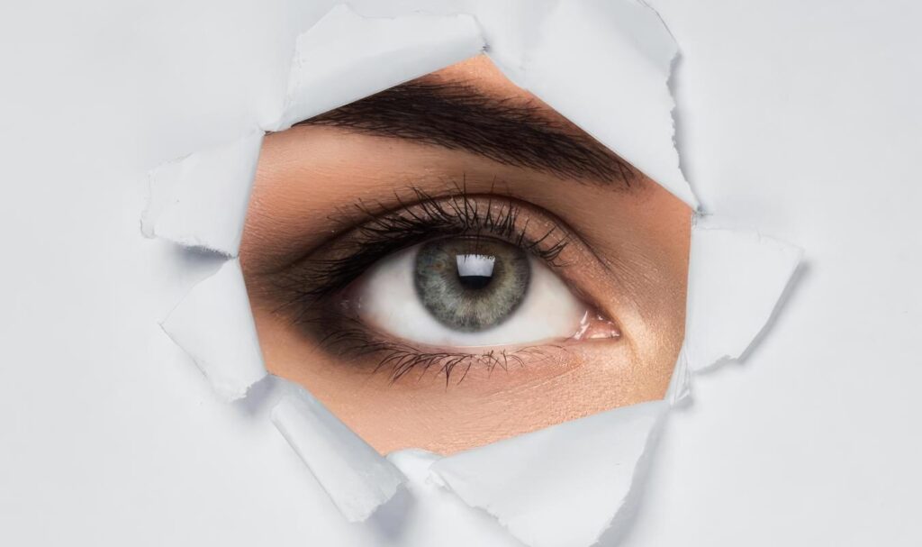 Close-up of a human eye looking through torn paper, representing focus and awareness