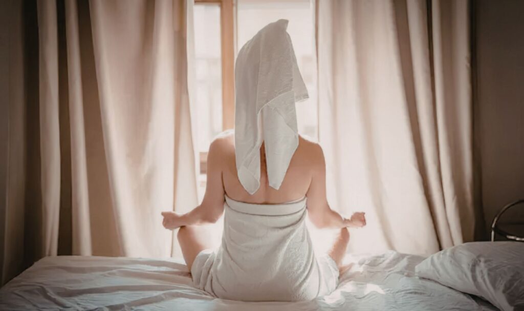 Woman sitting in bed at sunrise practicing morning meditation in a calm, minimalist bedroom