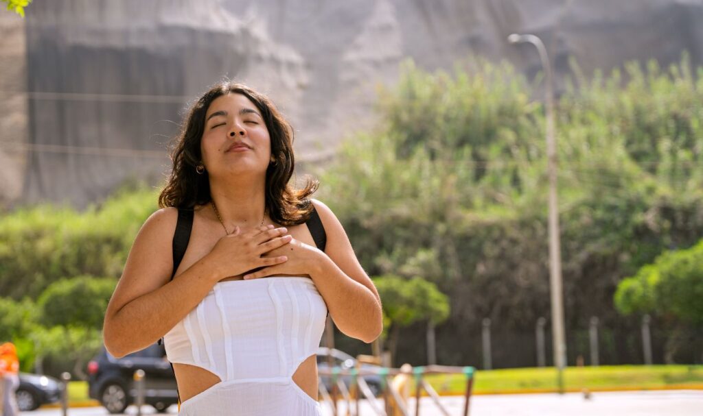 A happy and calm young woman holding her hands over her heart, symbolizing that she's overcome constant overstimulation.